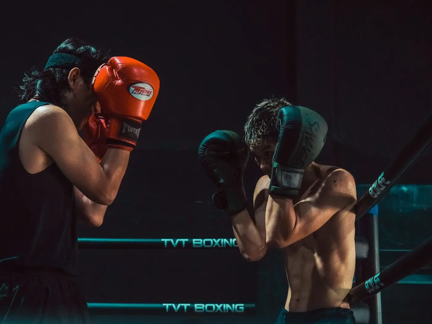 Young boxers in gloves and headguards training in a ring during an evening batch with a coach