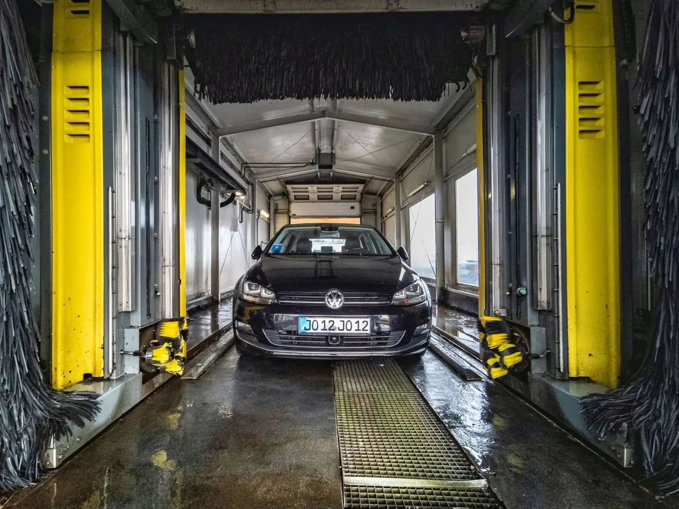 Car being foam washed in a covered bay while the owner books the next slot on a phone