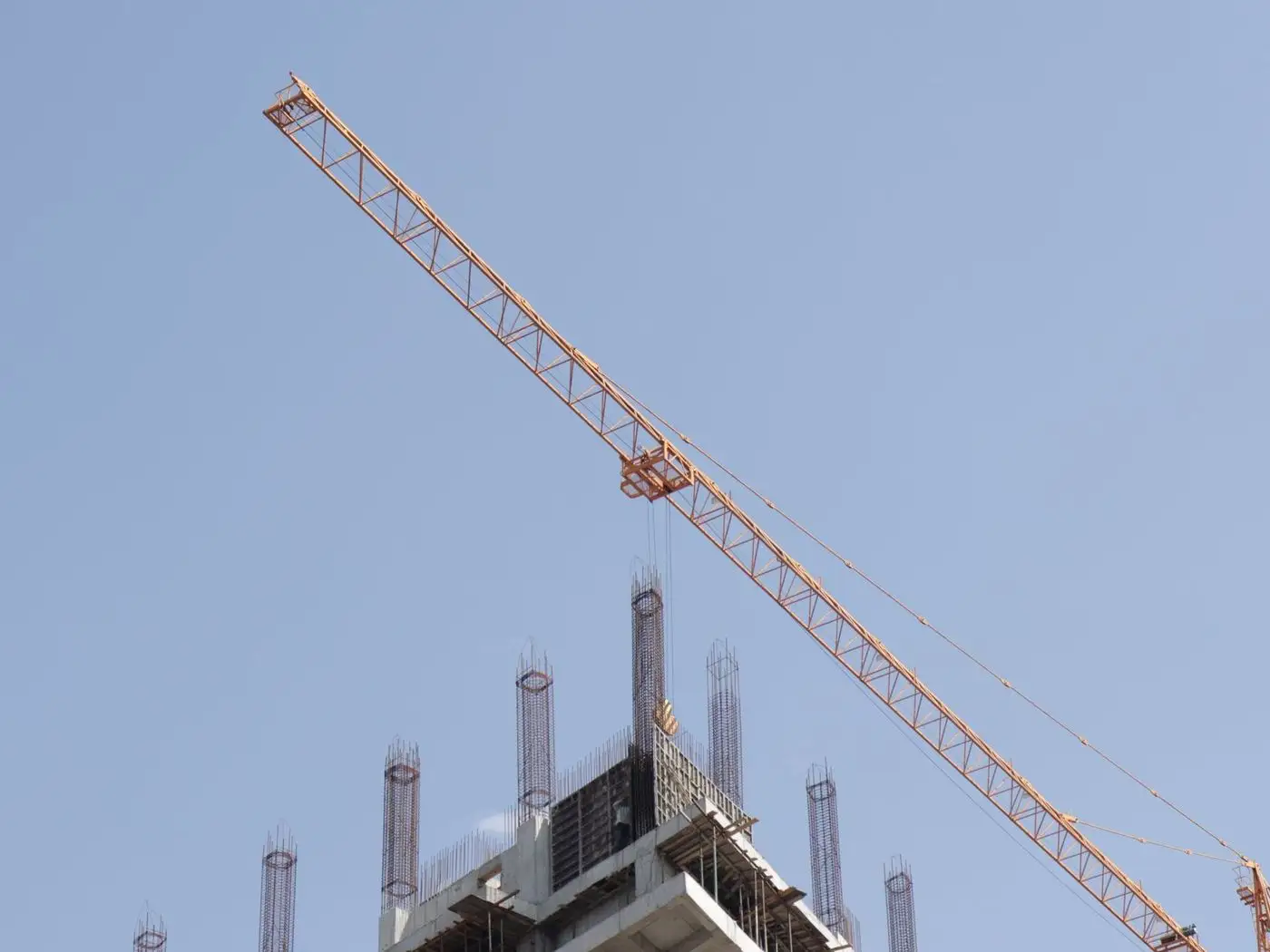 Truck-mounted mobile crane lifting a steel beam at an industrial building site with a supervisor checking a phone
