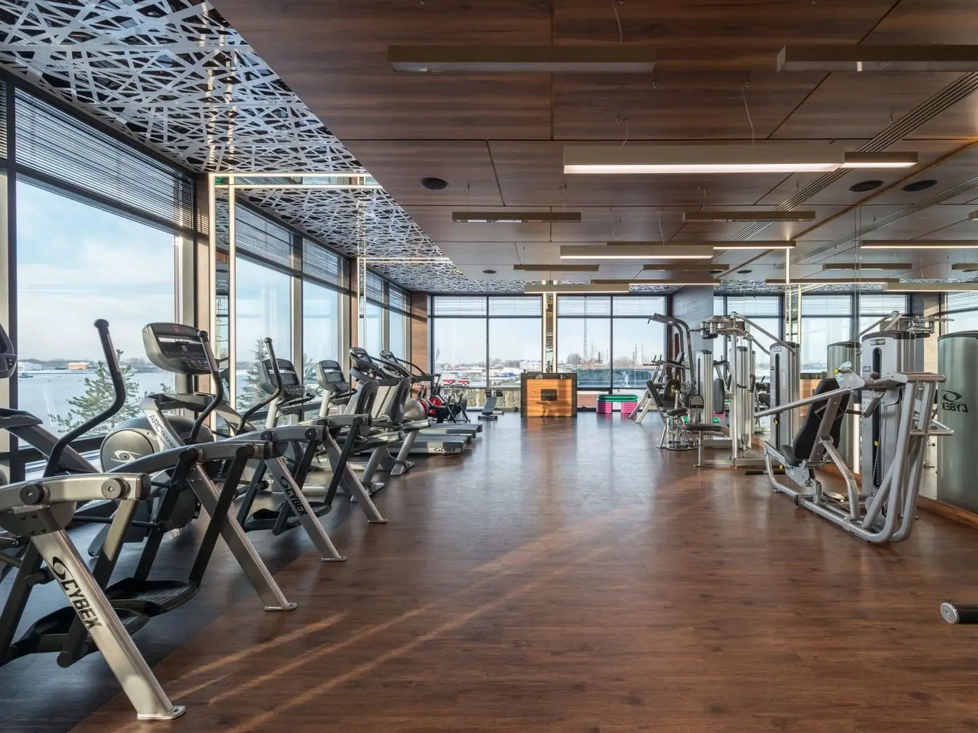 Bright gym floor with racks and a group class in progress, seen through glass doors from a reception desk