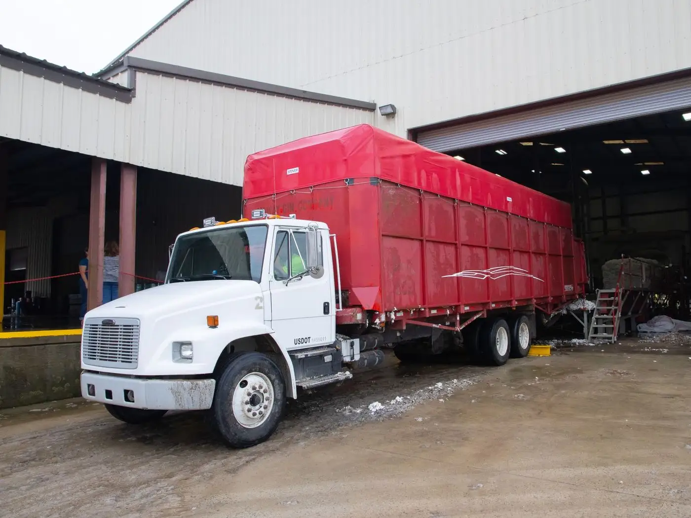 Workers loading cartons and machinery parts onto a truck at an industrial shed