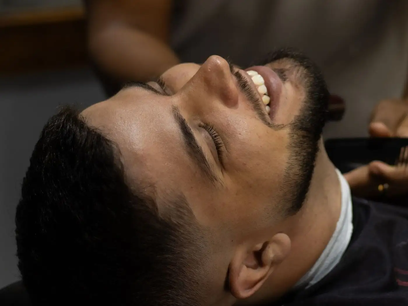 Busy unisex salon with a barber trimming a man's beard on one side and a stylist setting a woman's hair on the other