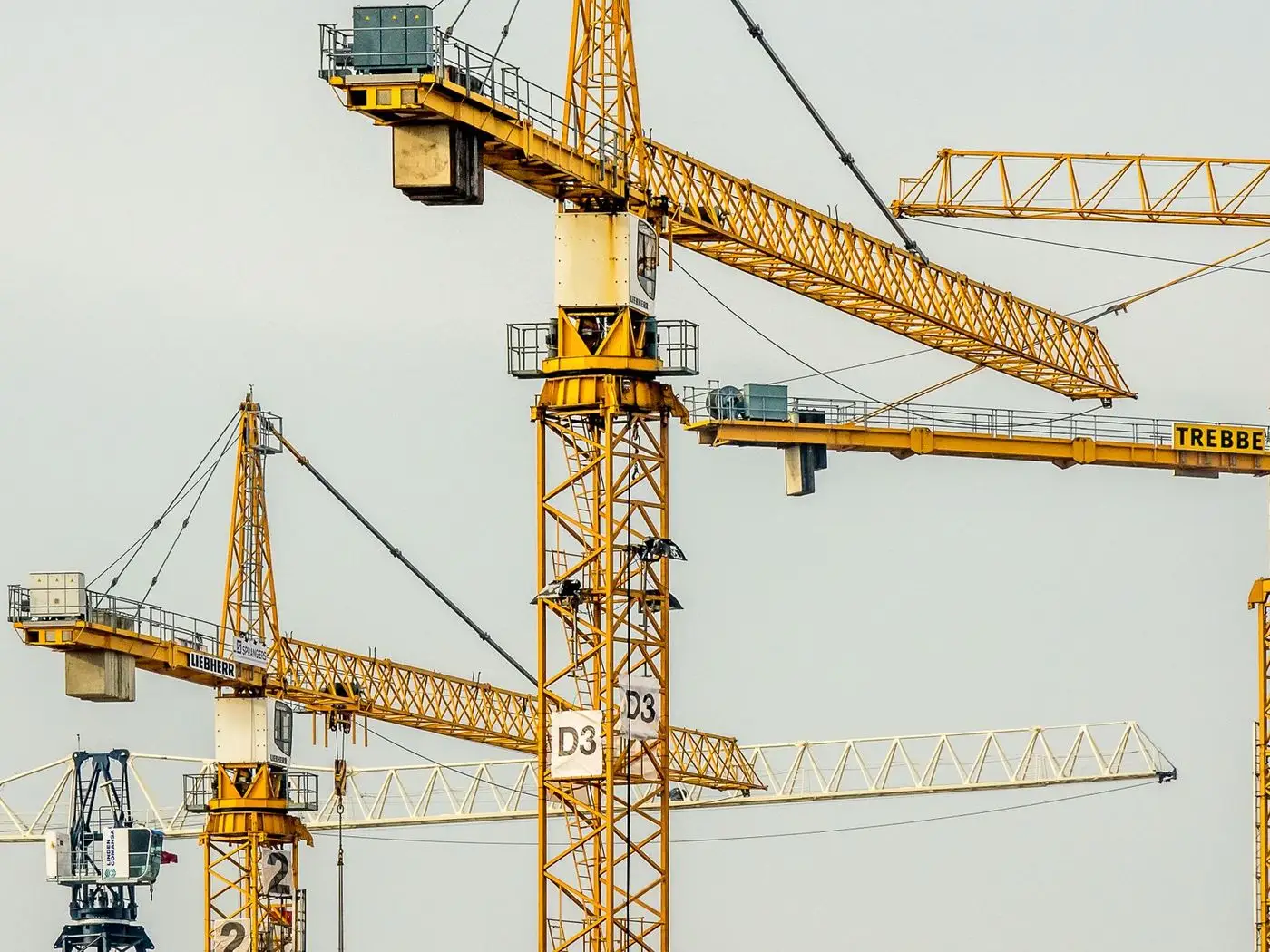 Truck-mounted mobile crane lifting a steel beam at an industrial site while a supervisor checks a phone