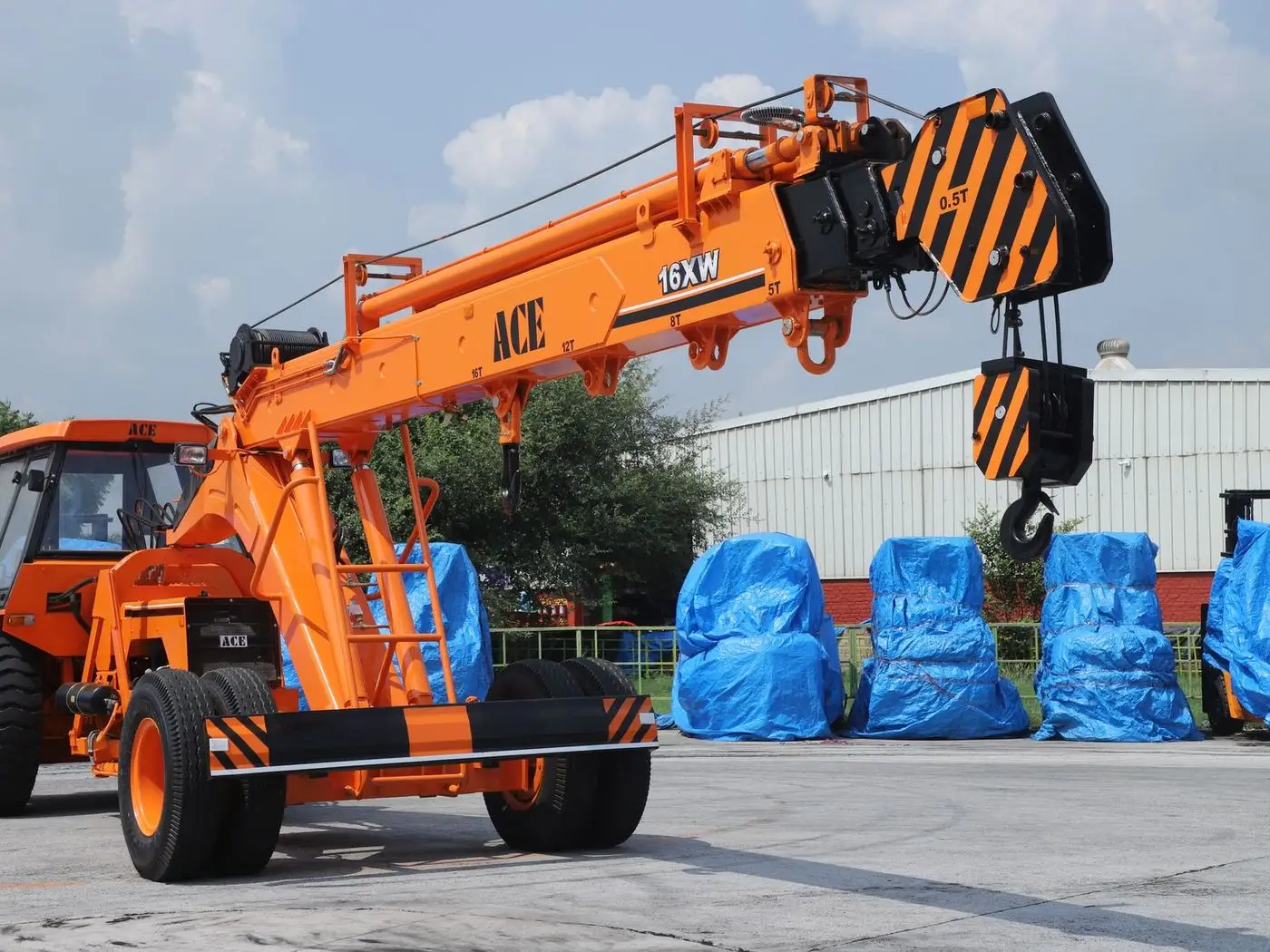 Truck-mounted mobile crane lifting a steel beam at an industrial site while a supervisor checks a phone